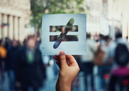 Eine Hand hält einen Papierzettel. Der Hintergrund ist verschwommen. Auf dem Zettel ist ein durchgestrichenes Gleichheits-Zeichen ausgeschnitten.